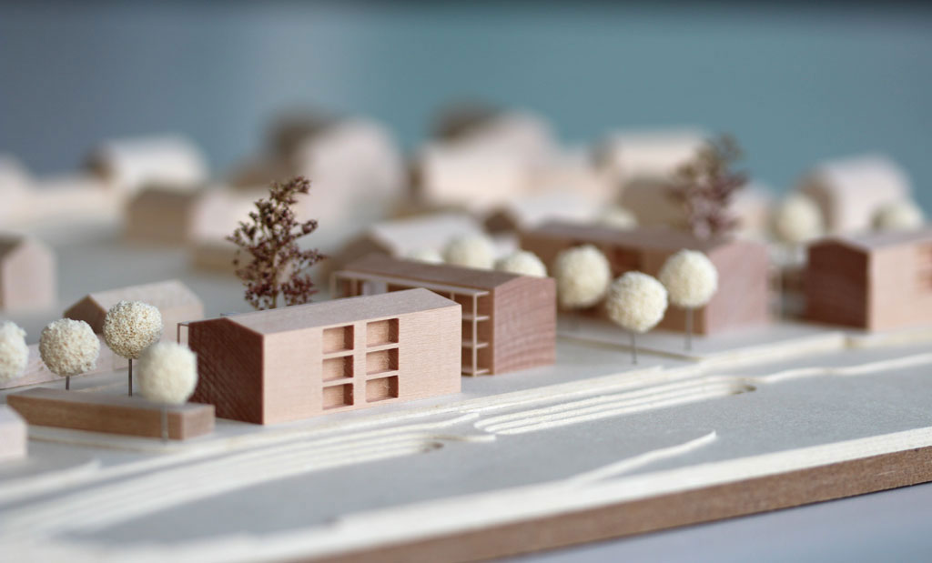 Architekturmodell mit Gebäuden aus Holz, Höhenschichten aus Finnpappe. Die Umgebungsgebäude sind vereinfacht dargestellt, die neue Planung detaillierter mit vorgestellten Laubengängen, Aufzügen und eingefrästen Loggien. Im Bereich des überplanten Gebietes sind Bäume aus Schwammgummikugeln und getrocknetem Seemoos gesetzt.
