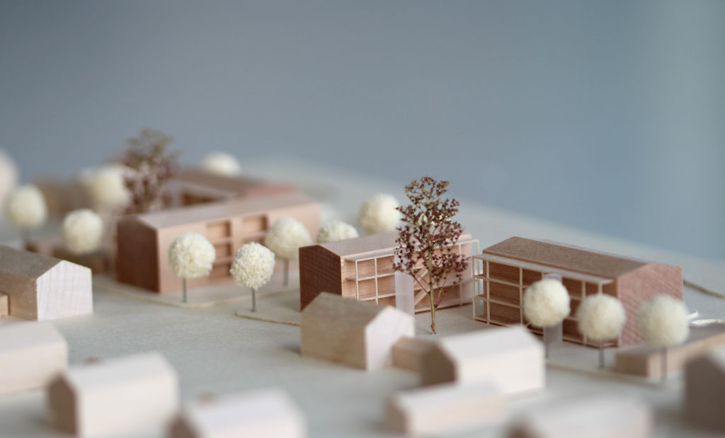 Architekturmodell mit Gebäuden aus Holz, Höhenschichten aus Finnpappe. Die Umgebungsgebäude sind vereinfacht dargestellt, die neue Planung detaillierter mit vorgestellten Laubengängen, Aufzügen und eingefrästen Loggien. Im Bereich des überplanten Gebietes sind Bäume aus Schwammgummikugeln und getrocknetem Seemoos gesetzt.