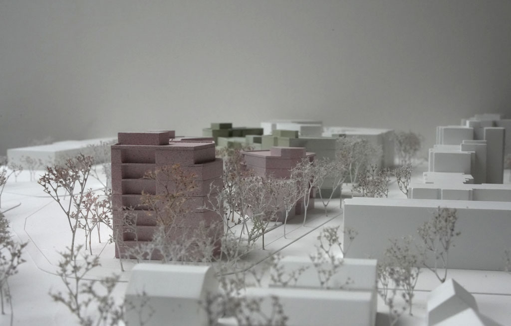 Das Foto zeigt ein Architekturmodell mit weißer Umgebung. Die neugeplanten Baukörper sind mehrgeschossige Volumina mit auskragenden Balkonen und verschiedenen Grün- und Rosatönen