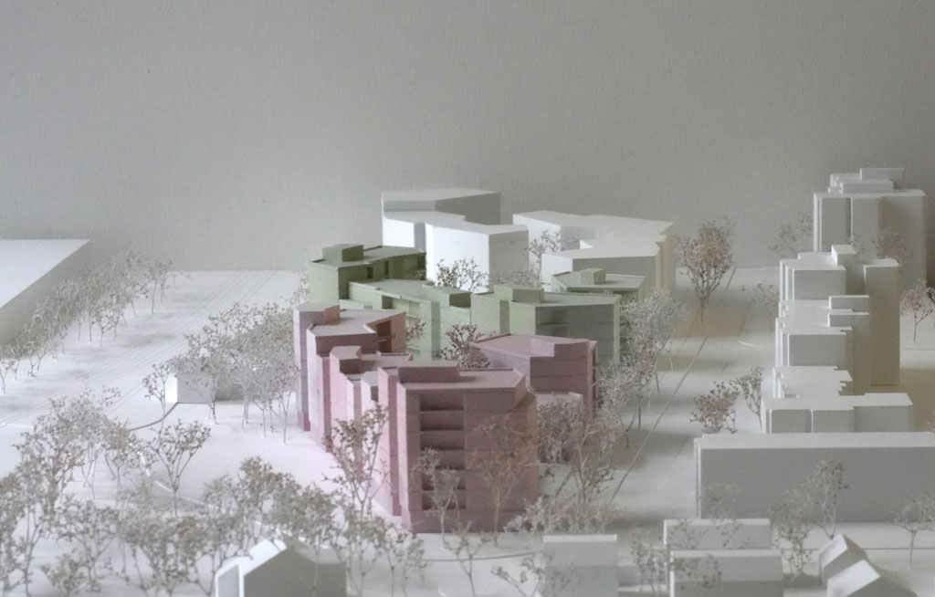 Das Foto zeigt ein Architekturmodell mit weißer Umgebung. Die neugeplanten Baukörper sind mehrgeschossige Volumina mit auskragenden Balkonen und verschiedenen Grün- und Rosatönen