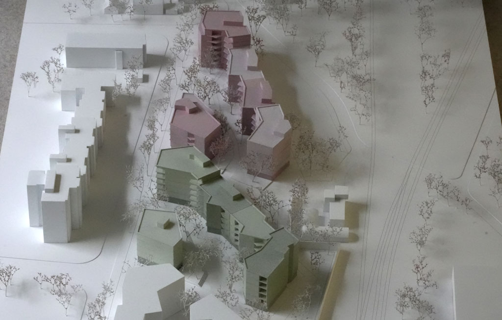 Das Foto zeigt ein Architekturmodell mit weißer Umgebung. Die neugeplanten Baukörper sind mehrgeschossige Volumina mit auskragenden Balkonen und verschiedenen Grün- und Rosatönen