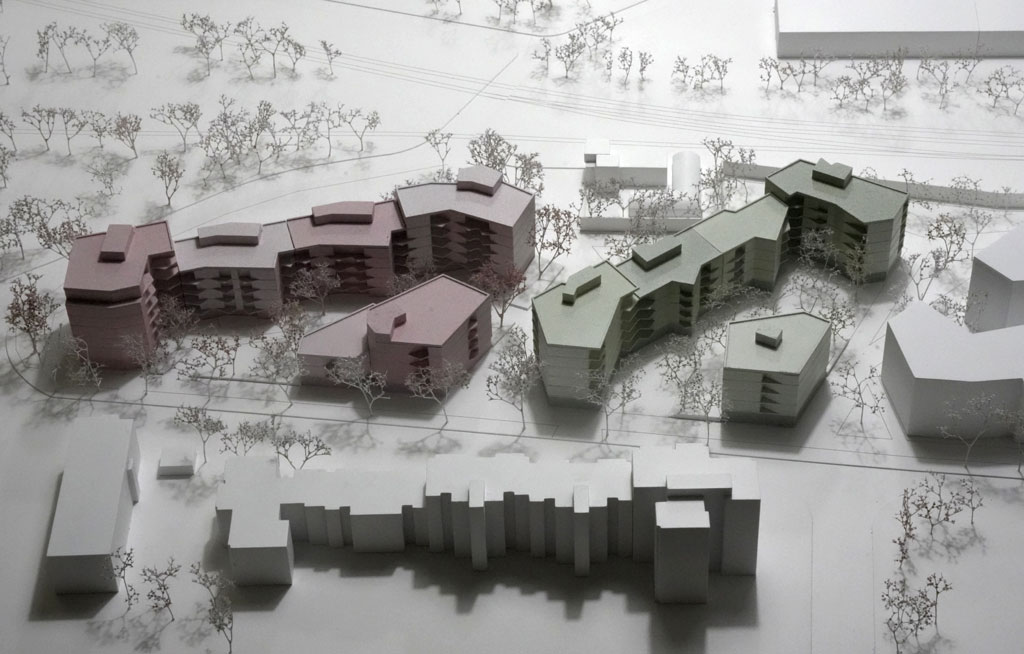 Das Foto zeigt ein Architekturmodell mit weißer Umgebung. Die neugeplanten Baukörper sind mehrgeschossige Volumina mit auskragenden Balkonen und verschiedenen Grün- und Rosatönen