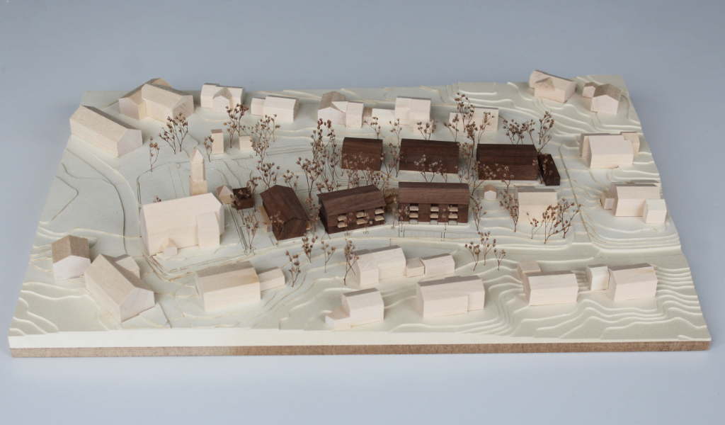 Architekturmodell mit Höhenschichten aus gelblicher Finnpappe, Gebäuden aus Linden- und Nussbaumholz. Die neu geplanten Wohngebäude sind aus Nussbaumholz mit eingefrästen Loggien. Die Balkonflächen sind aus hellem Birkenholz.