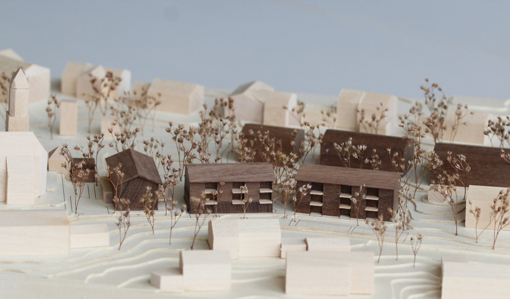 Architekturmodell mit Höhenschichten aus gelblicher Finnpappe, Gebäuden aus Linden- und Nussbaumholz. Die neu geplanten Wohngebäude sind aus Nussbaumholz mit eingefrästen Loggien. Die Balkonflächen sind aus hellem Birkenholz.