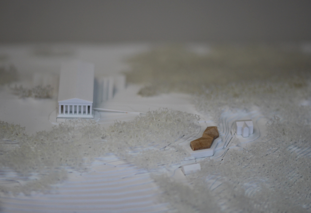 weißes Architekturmodell von der Walhalla und Umgebung. Der Höhenverlauf ist mittels Höhenschichten dargestellt, zur Dargestellung der Bäume ist weißer Pflanzenschaum flächig verklebt. Der Neubau des Besucherzentrums liegt nordöstlich von der Walhalla und besteht aus einem weißen Sockel auf dem ein kleines Holzvolumen mit mehreren Dachverschneidungen sitzt. Draufsicht von Norden. Nanaufnahme.