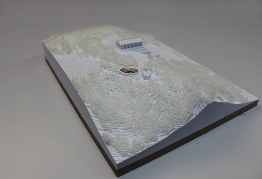 weißes Architekturmodell von der Walhalla und Umgebung. Der Höhenverlauf ist mittels Höhenschichten dargestellt, zur Dargestellung der Bäume ist weißer Pflanzenschaum flächig verklebt. Der Neubau des Besucherzentrums liegt nordöstlich von der Walhalla und besteht aus einem weißen Sockel auf dem ein kleines Holzvolumen mit mehreren Dachverschneidungen sitzt. Draufsicht von Nordosten.