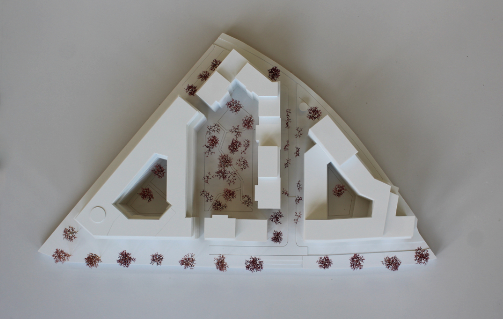 weißes architektonisches Massenmodell, bestehend aus vier großen Baukörpern angeordnet auf einer dreiecksförmigen Grundplatte. Die Geschosse der Baukörper sind ablesbar, da die Geschossdecken minimal auskragen. Die Bäume sind aus getrocknetem Pflanzenmaterial dargestellt. Das Modell ist von schräg oben fotografiert.