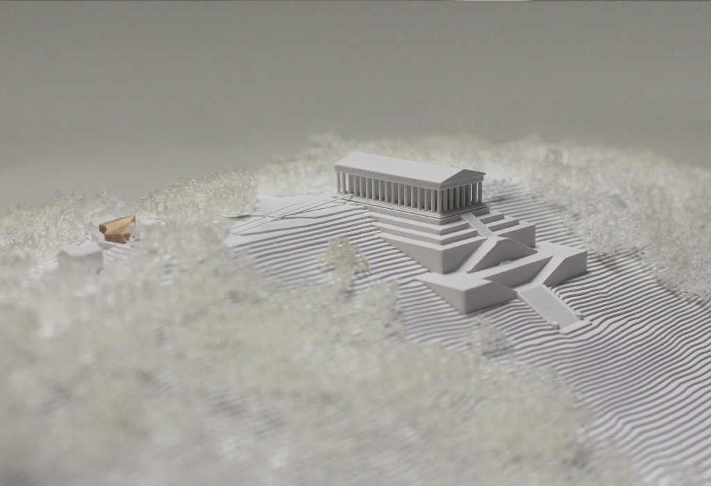 weißes Architekturmodell von der Walhalla und Umgebung. Der Höhenverlauf ist mittels Höhenschichten dargestellt, zur Dargestellung der Bäume ist weißer Pflanzenschaum flächig verklebt. Der Neubau des Besucherzentrums liegt nordöstlich von der Walhalla und besteht aus einem weißen Sockel auf dem ein kleines Holzvolumen mit mehreren Dachverschneidungen sitzt. Draufsicht von Süden.